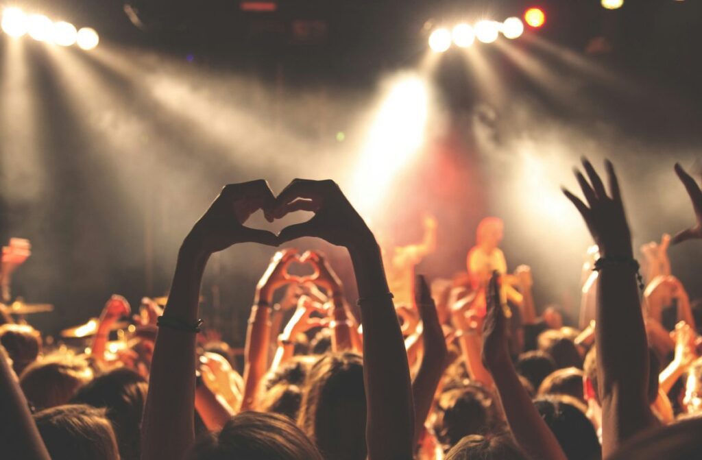 Person holding up hand heart at a music festival.